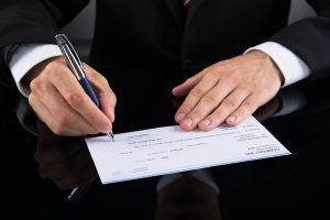 bigstock-Businessperson-Signing-Cheque-100578386-300x200